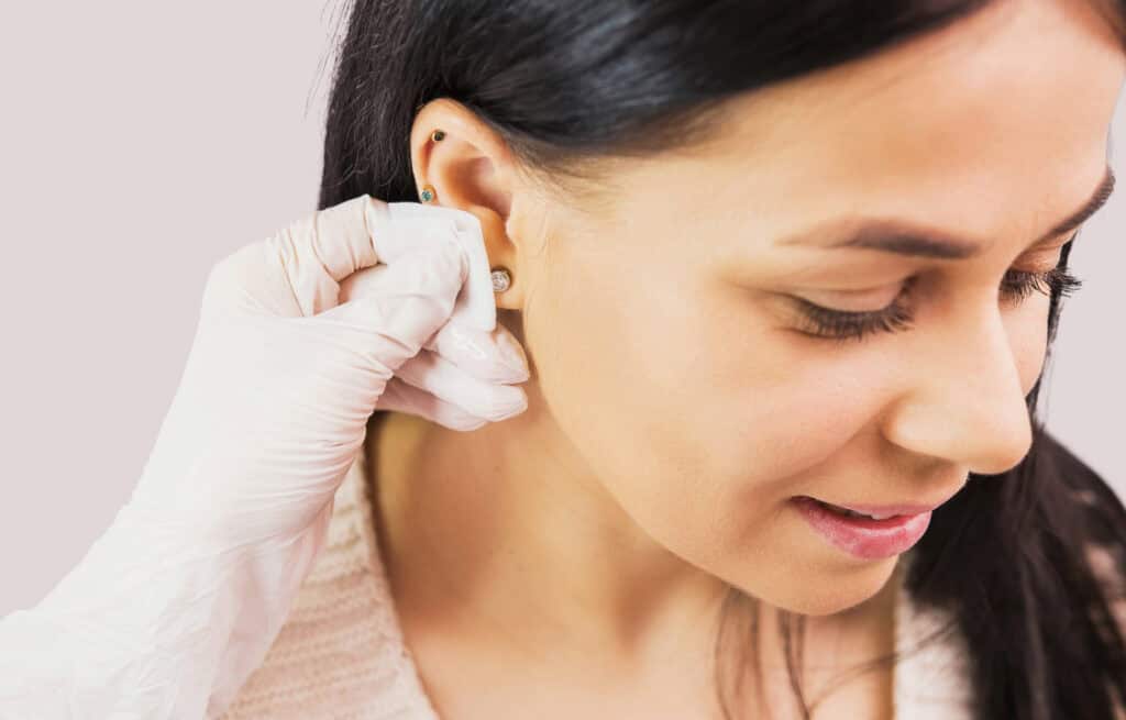 Close-up of woman getting her ear pierced. Addresses the question 'Can you get piercings while pregnant?'