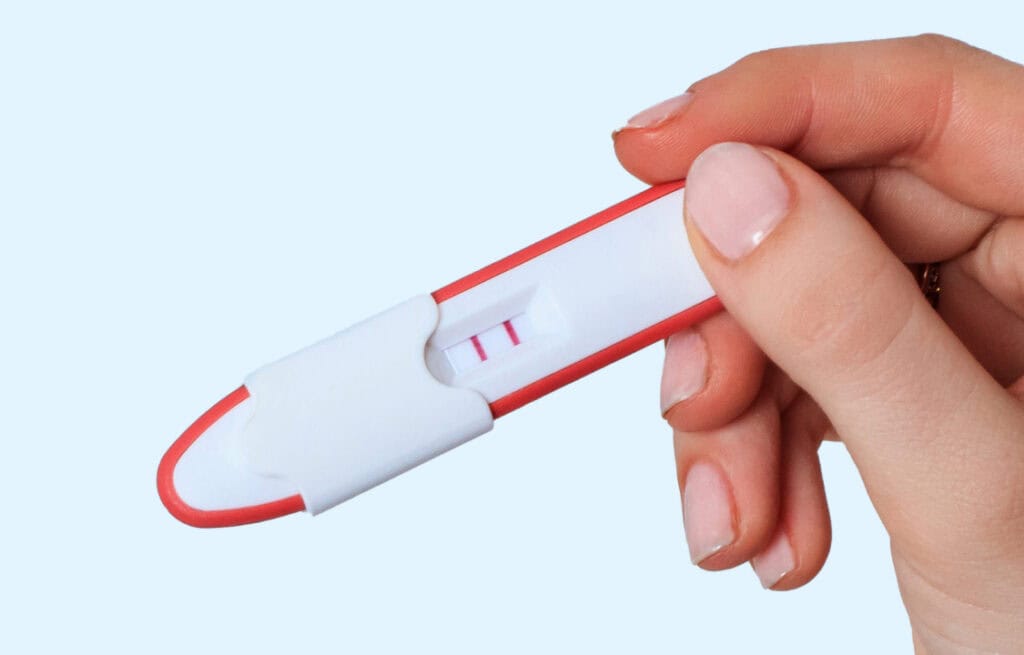 Hand holding a positive pregnancy test with two lines. Can you get pregnant during perimenopause? This image relates to that question.