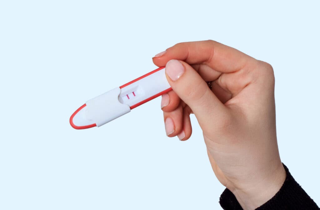 Hand holding a positive pregnancy test with two lines. Can you get pregnant during perimenopause? This image relates to that question.