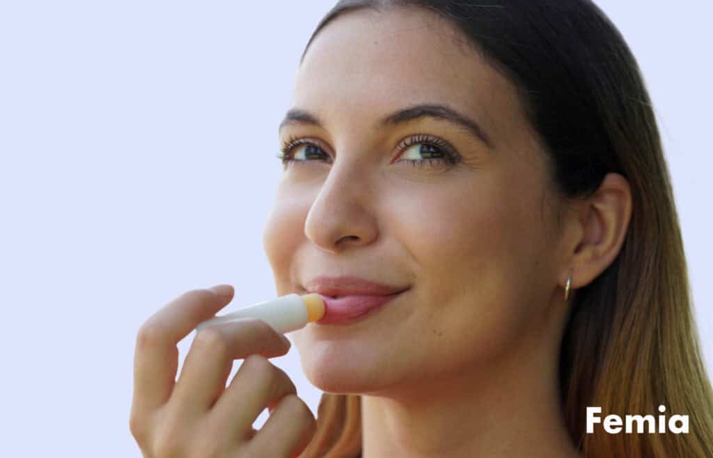 A woman smiling while applying lip balm as an alternative to getting lip fillers while pregnant.