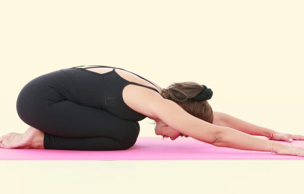 A woman in a child's pose, practicing reverse Kegels.