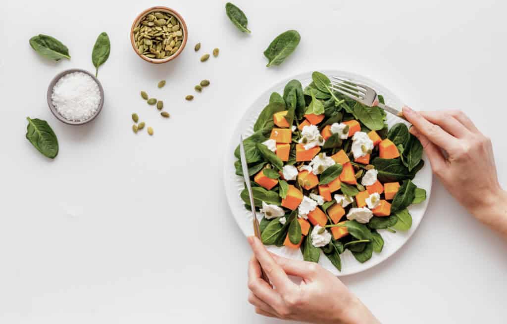 Photo of a healthy meal plate with greens, pumpkin, goat cheese, and seeds.