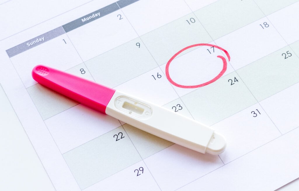 A pregnancy test placed on a calendar with a date circled in red.