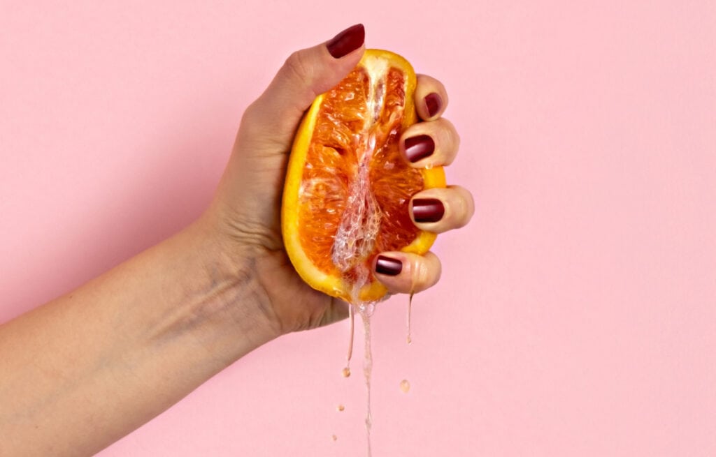 A hand squeezing a juicy orange, symbolizing the concept of squirting.