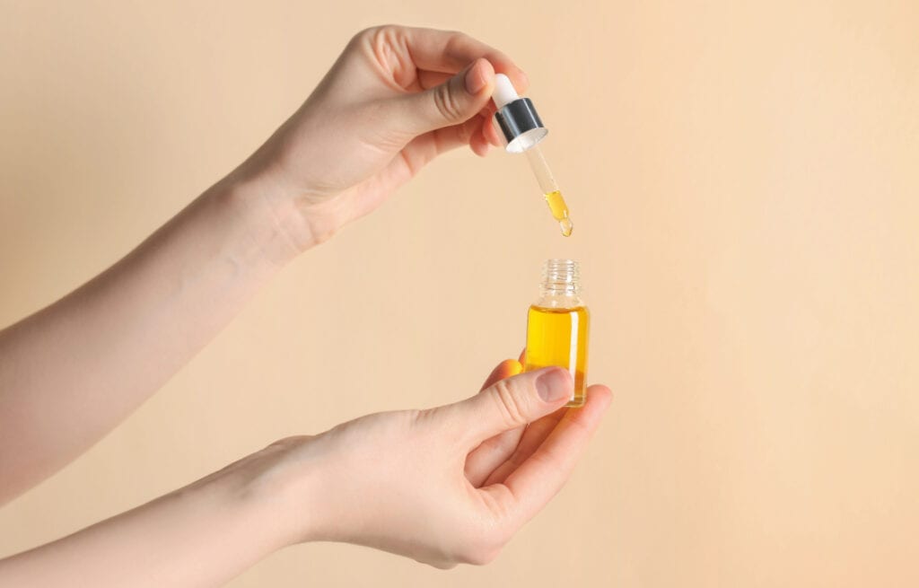 Hands holding a dropper bottle with oil, preparing for perineal massage.