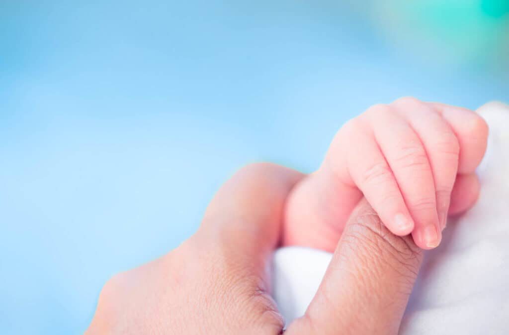 A picture of a premature baby holding mom's thumb.