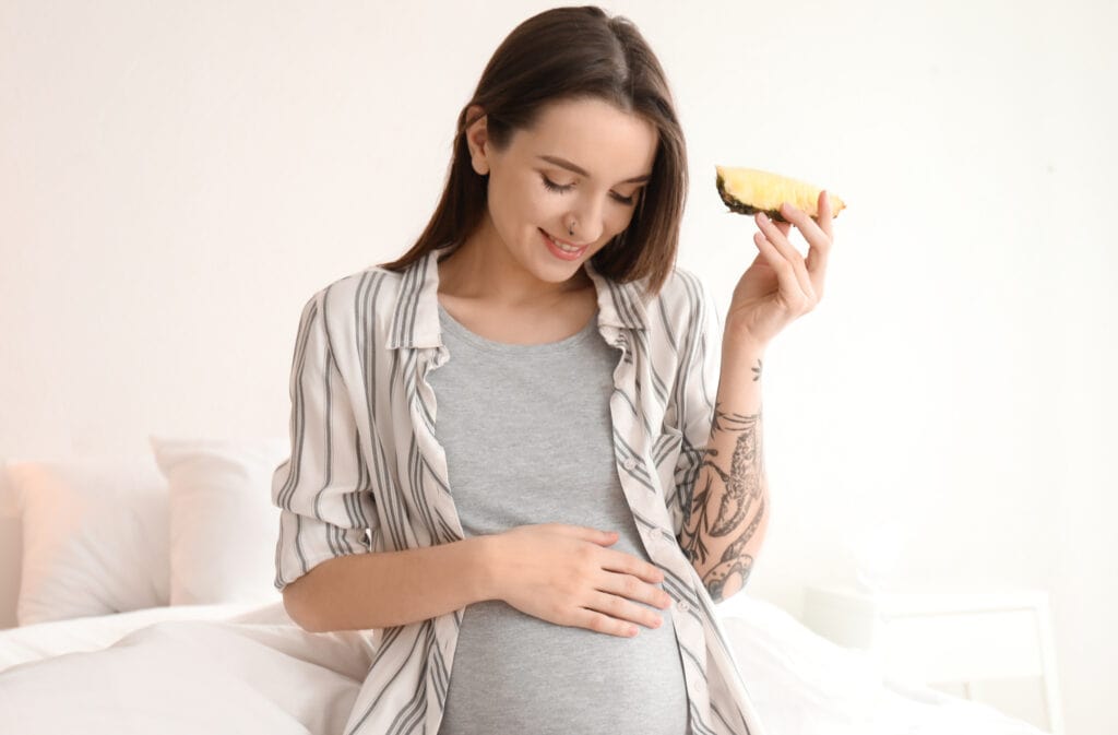 A photo of a pregnant woman eating a pineapple.