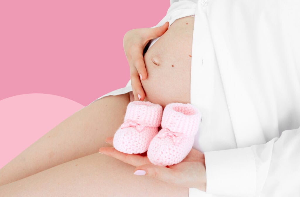 A photo of a pregnant belly with pink baby shoes, representing the question of how to conceive a girl?