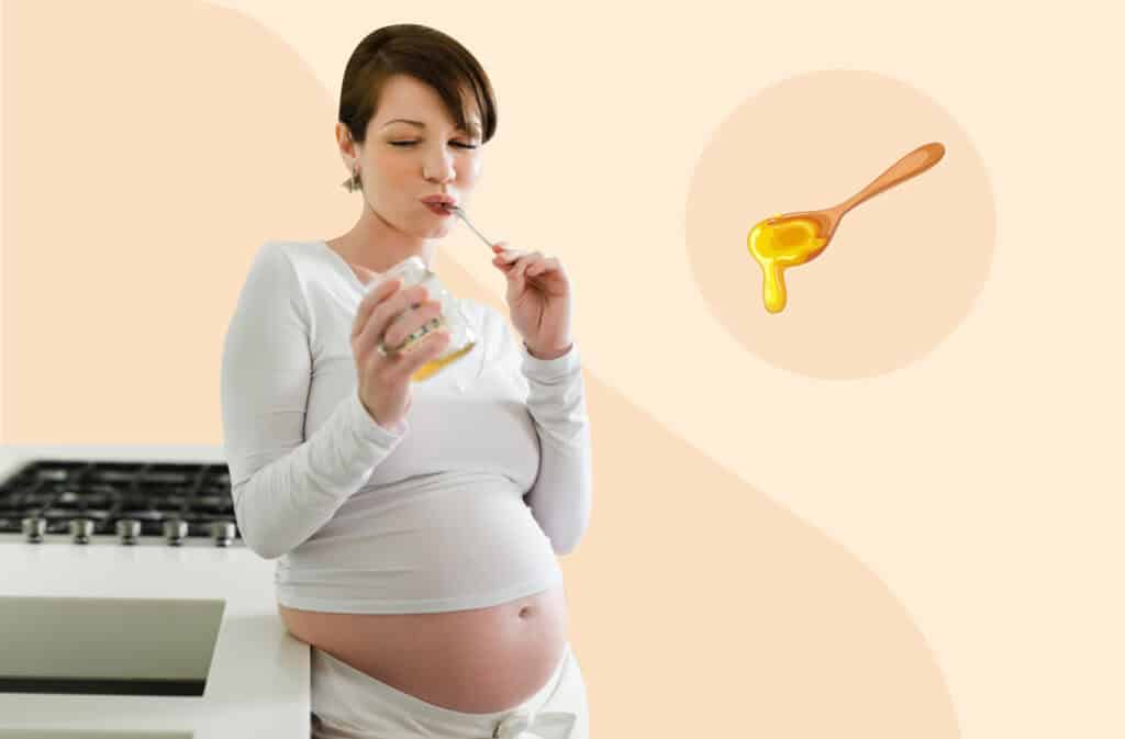 A photo of a pregnant woman standing by the stove and eating honey with a spoon while wondering 'Can you eat honey while pregnant?'.