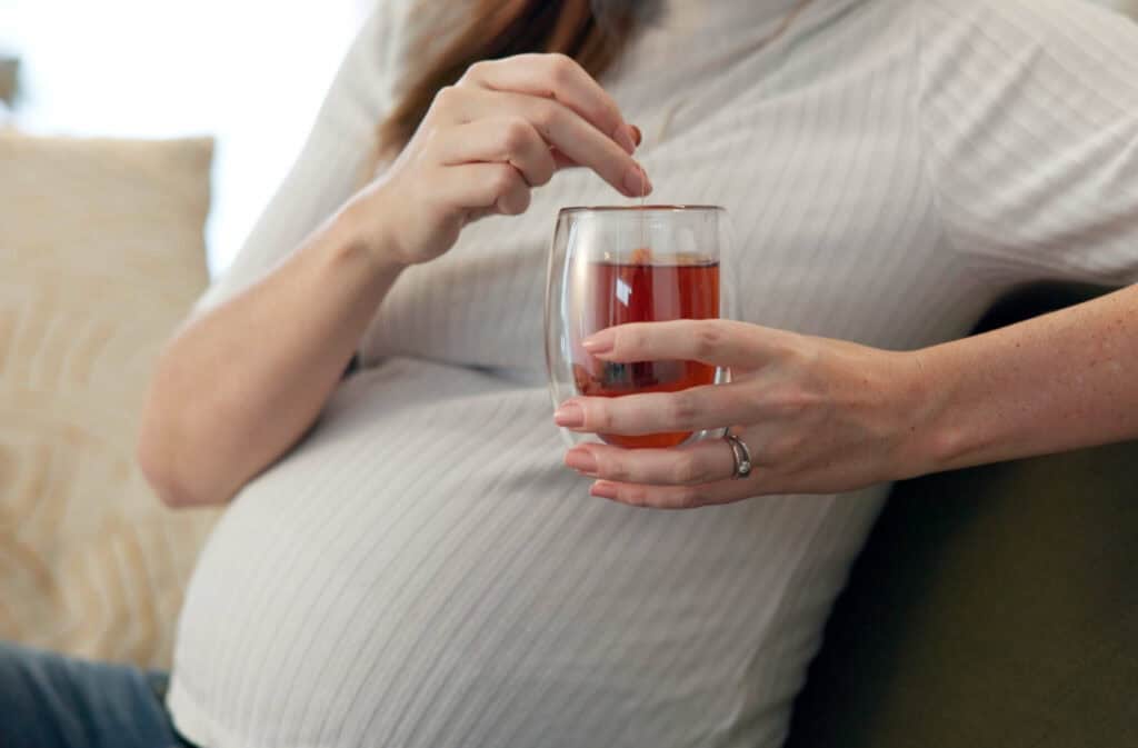 A photo of a pregnant woman holding a cup of tea representing the question 'Can you drink tea while pregnant'.