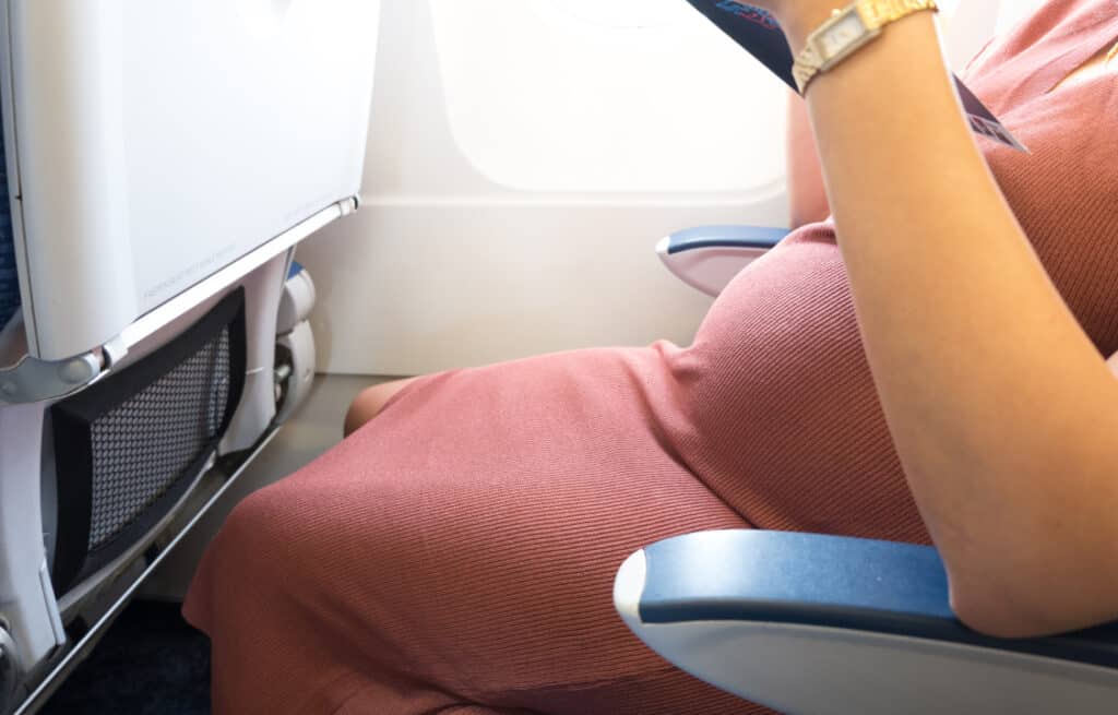 A photo of a woman sitting in an aircraft and wondering 'Is it safe to fly while pregnant?'.