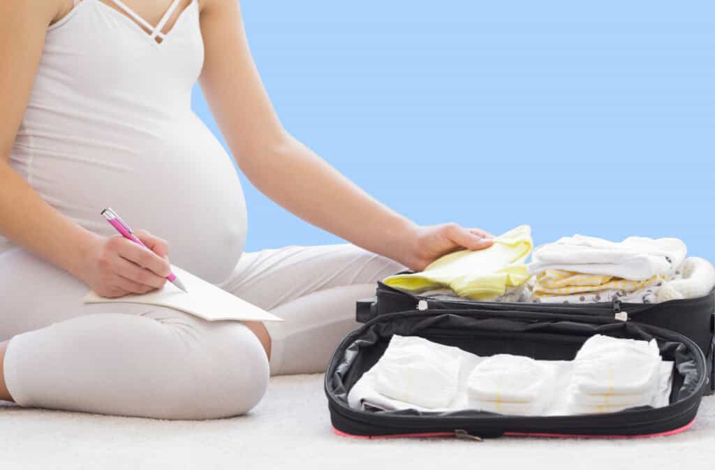 A photo of a pregnant woman packing a suitcase for labor and holding a hospital bag checklist for mom on her lap.