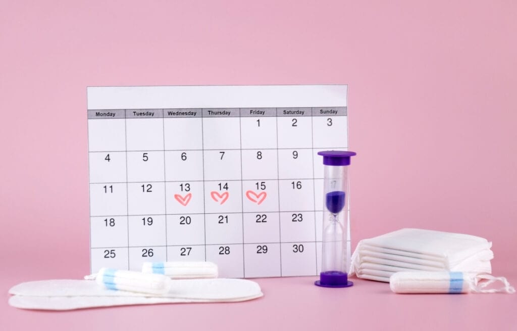 A photo of a calendar, pads, tampons and an hourglass, representing the question 'how to make your period come faster'