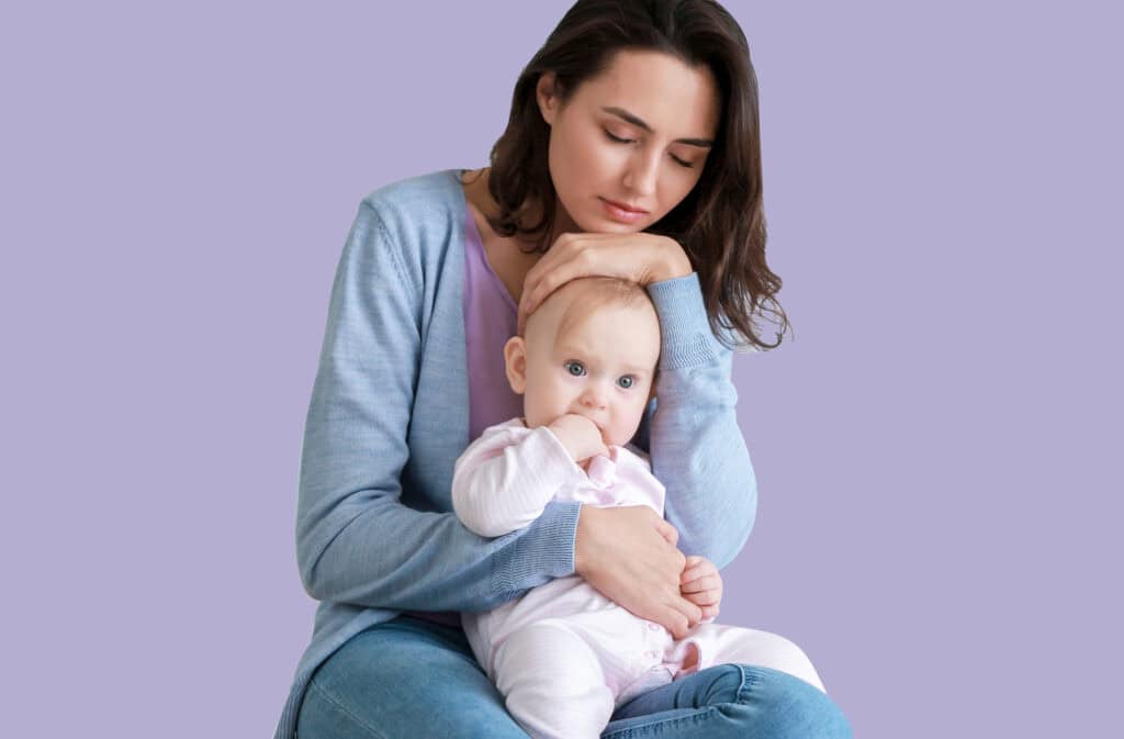 A photo of an overwhelmed mom holding a baby and probably experiencing postpartum anxiety.