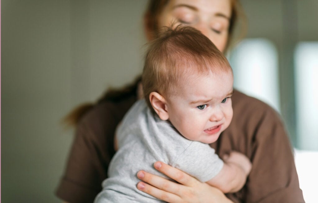 A photo of a mom holding an upset 7-month-old baby, experiencing 7-month sleep regression.