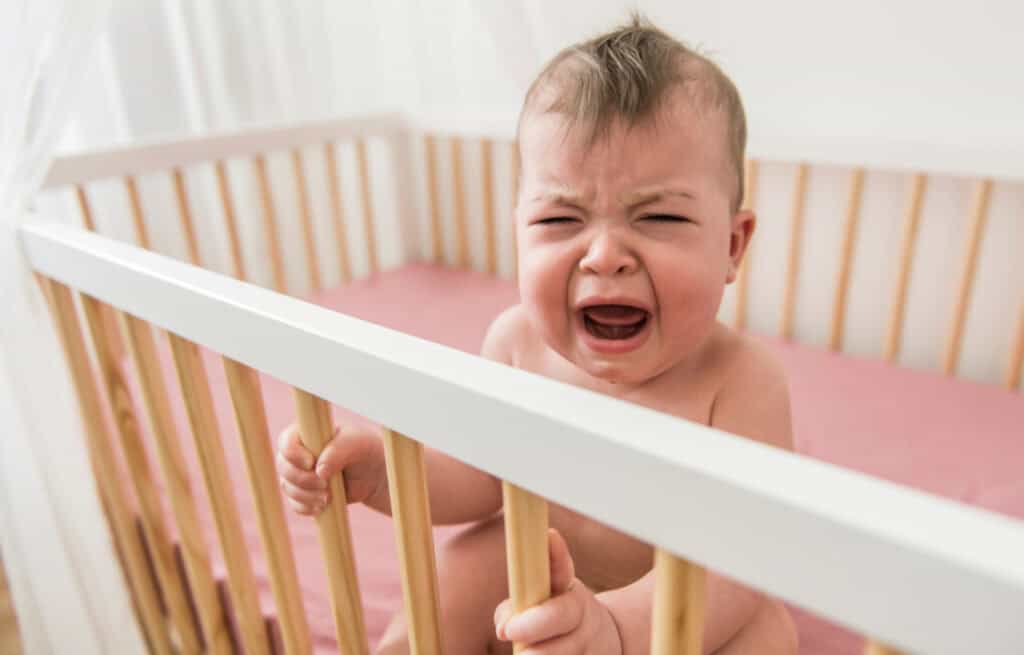 A photo of an upset 8-month-old baby in a crib, experiencing 8-month sleep regression.