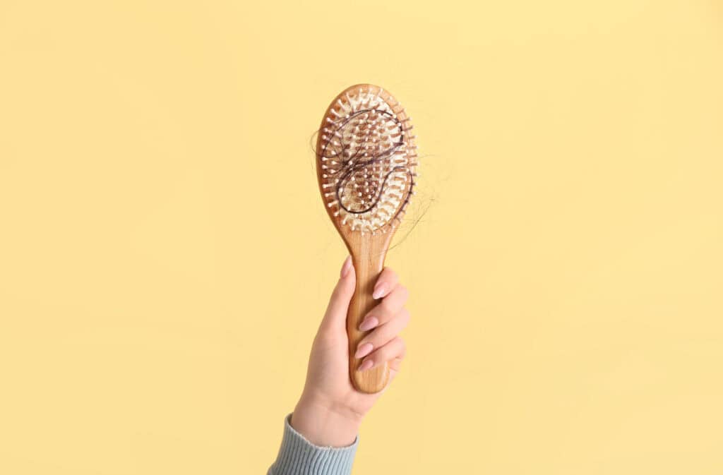 A photo of a hand, holding a brush covered in hair, representing postpartum hair loss.